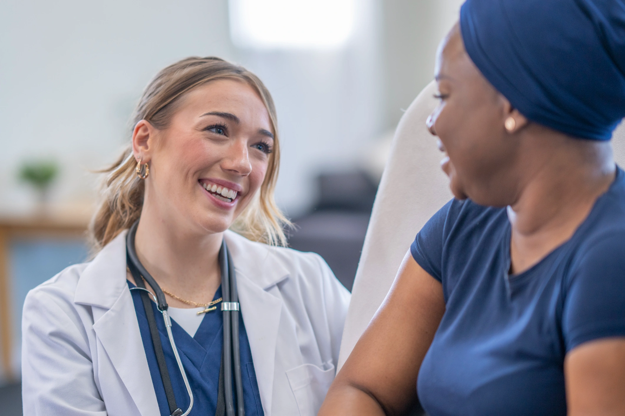 Smiling female doctor with a stethoscope conversing attentively with a patient wearing a headscarf.