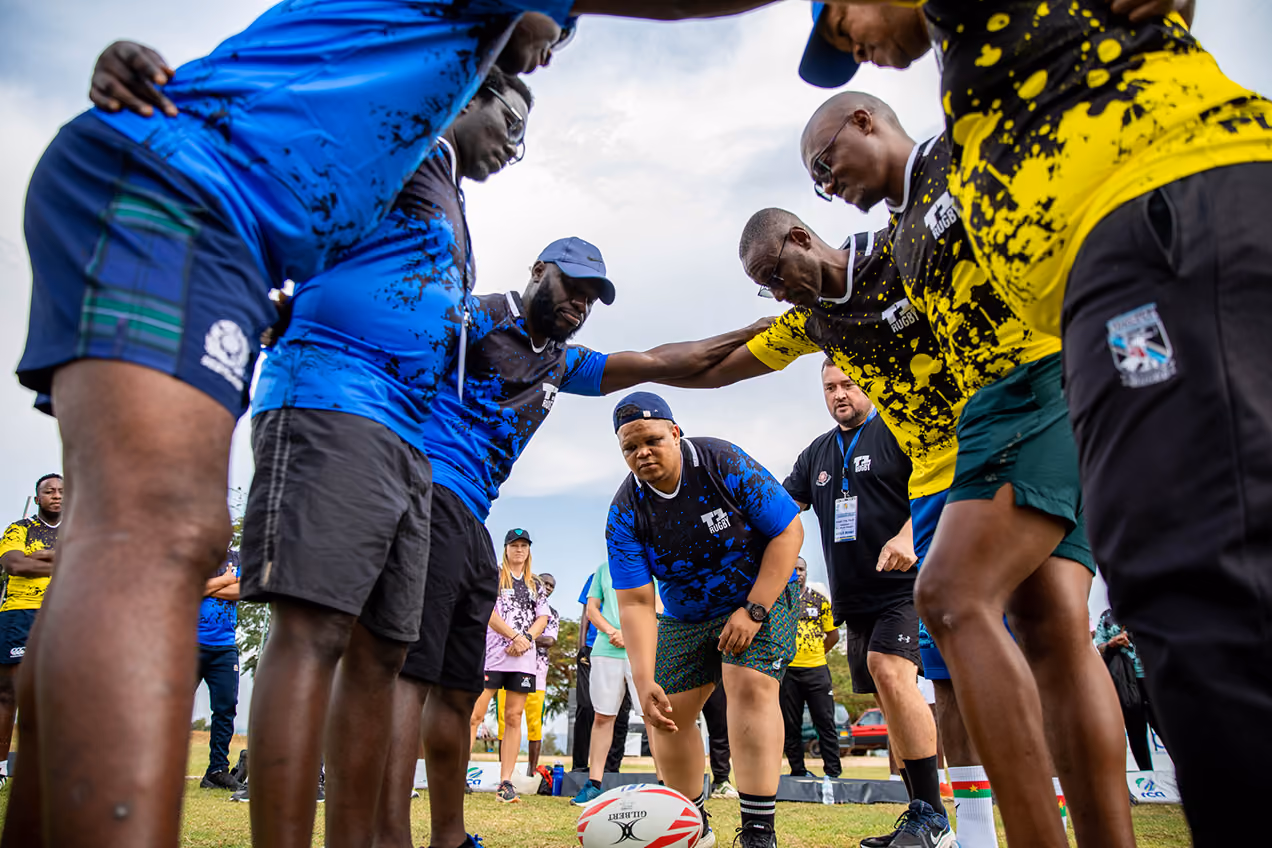 Rugby players in blue and yellow jerseys huddle closely around a rugby ball on grass.