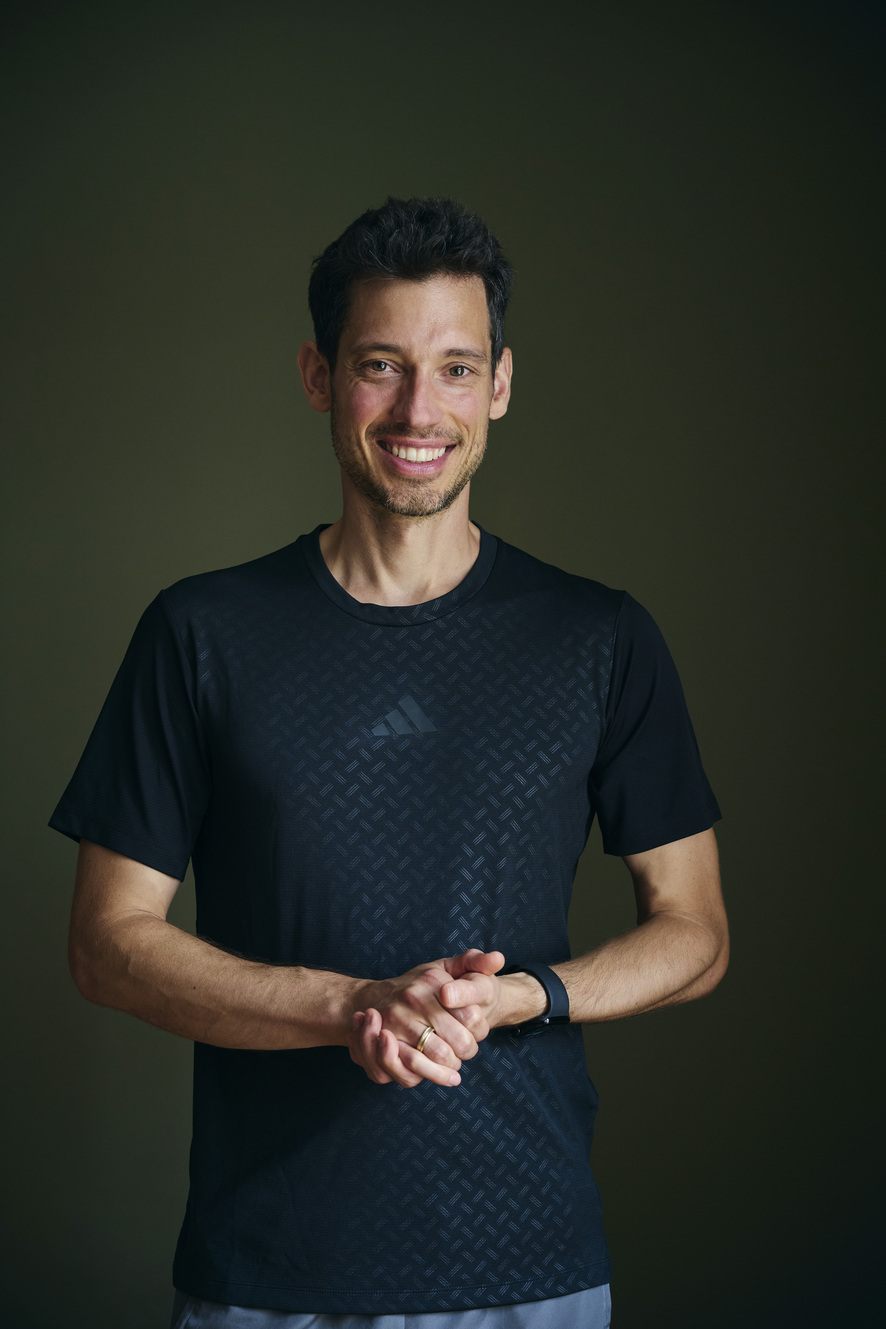 Sportwissenschaftler und Personal Trainer Lars Traxel in sportlicher Kleidung vor dunklem Hintergrund.