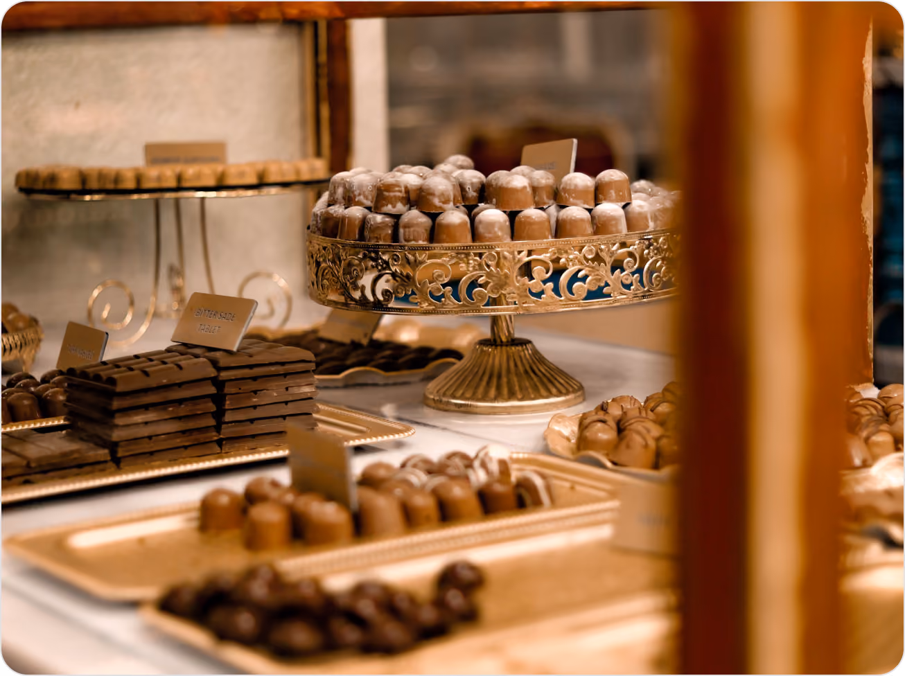 Assorted chocolates and chocolate bars displayed on ornate gold trays and a stand in a confectionery shop.