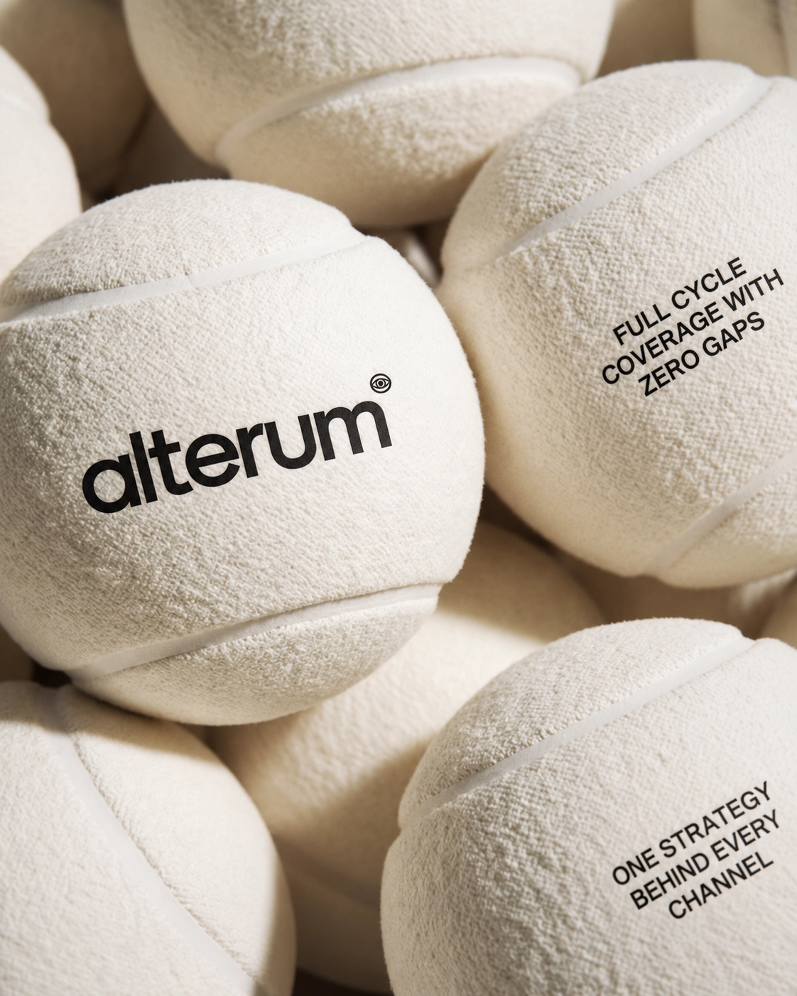 Close-up of several textured beige balls with white curved lines, one ball shows the word 'alterum' and another has the phrases 'FULL CYCLE COVERAGE WITH ZERO GAPS' and 'ONE STRATEGY BEHIND EVERY CHANNEL' in black text.