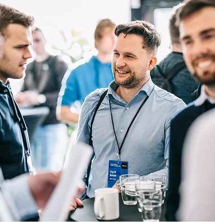 Tři muži v neformálním oblečení vedou rozhovor u stolu s nápoji na konferenci.