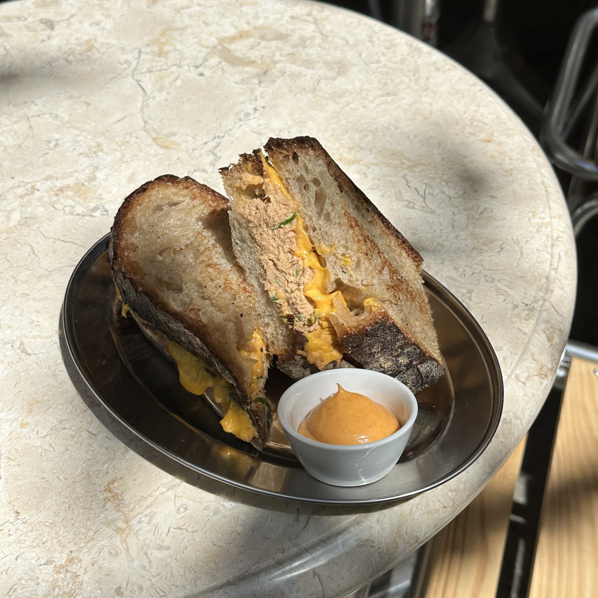 Aufgeschnittener Tuna Melt aus geröstetem Sauerteigbrot mit geschmolzenem Cheddar, dazu ein Schälchen Sauce