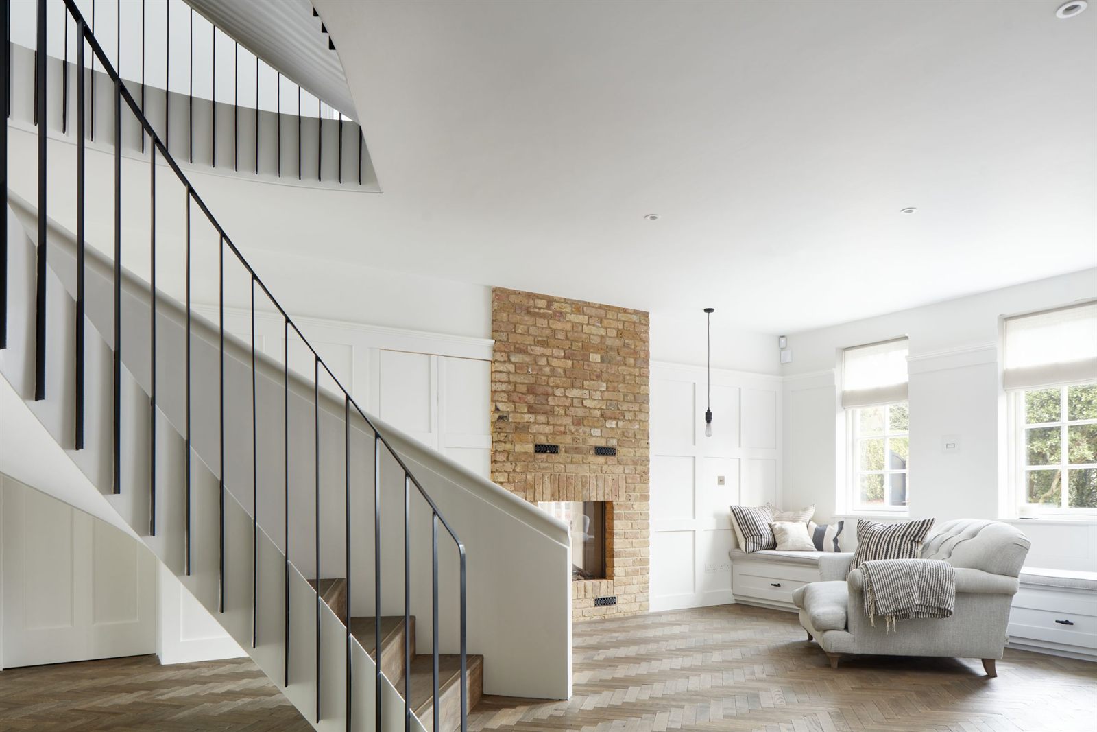 Double Act: a stair hall with a black steel balustrade and an exposed brick chimney breast, opening to the living room