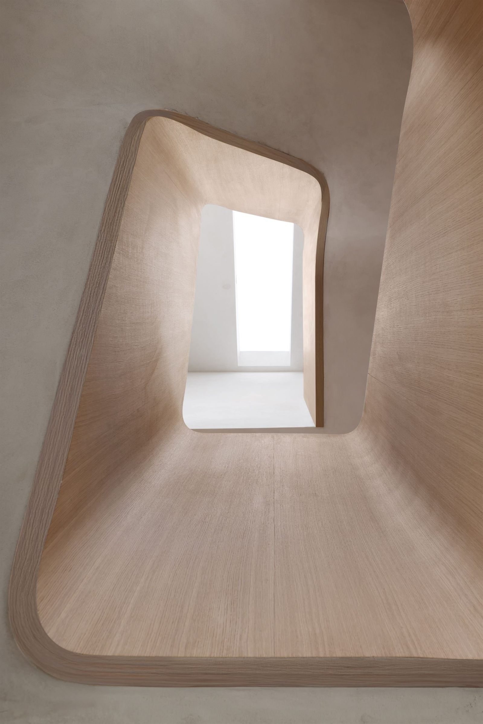 Looking up through the oak lined stairwell at Scenario Home, its curved timber edges framing a bright rooflight above
