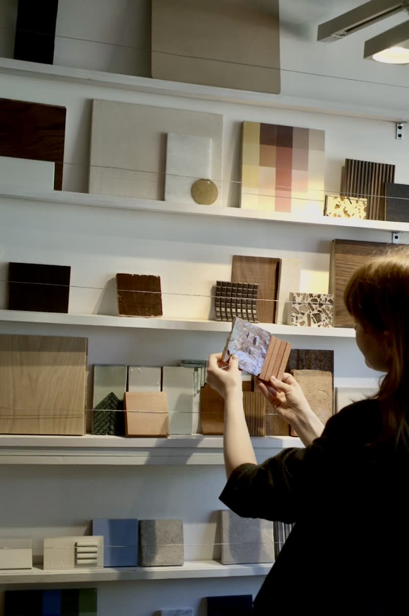 Someone holding a sample up against a wall of shelved material samples in timber, stone, terrazzo, tile and brick.