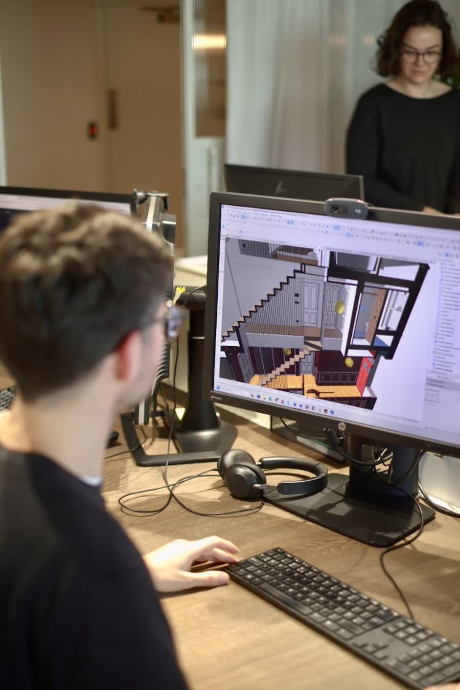 Someone modelling a staircase and interior in 3D on a large monitor, with a colleague standing behind.