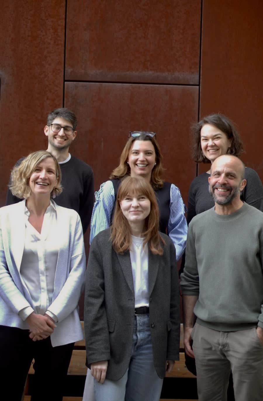 Six members of the team standing together in front of a weathered steel wall.
