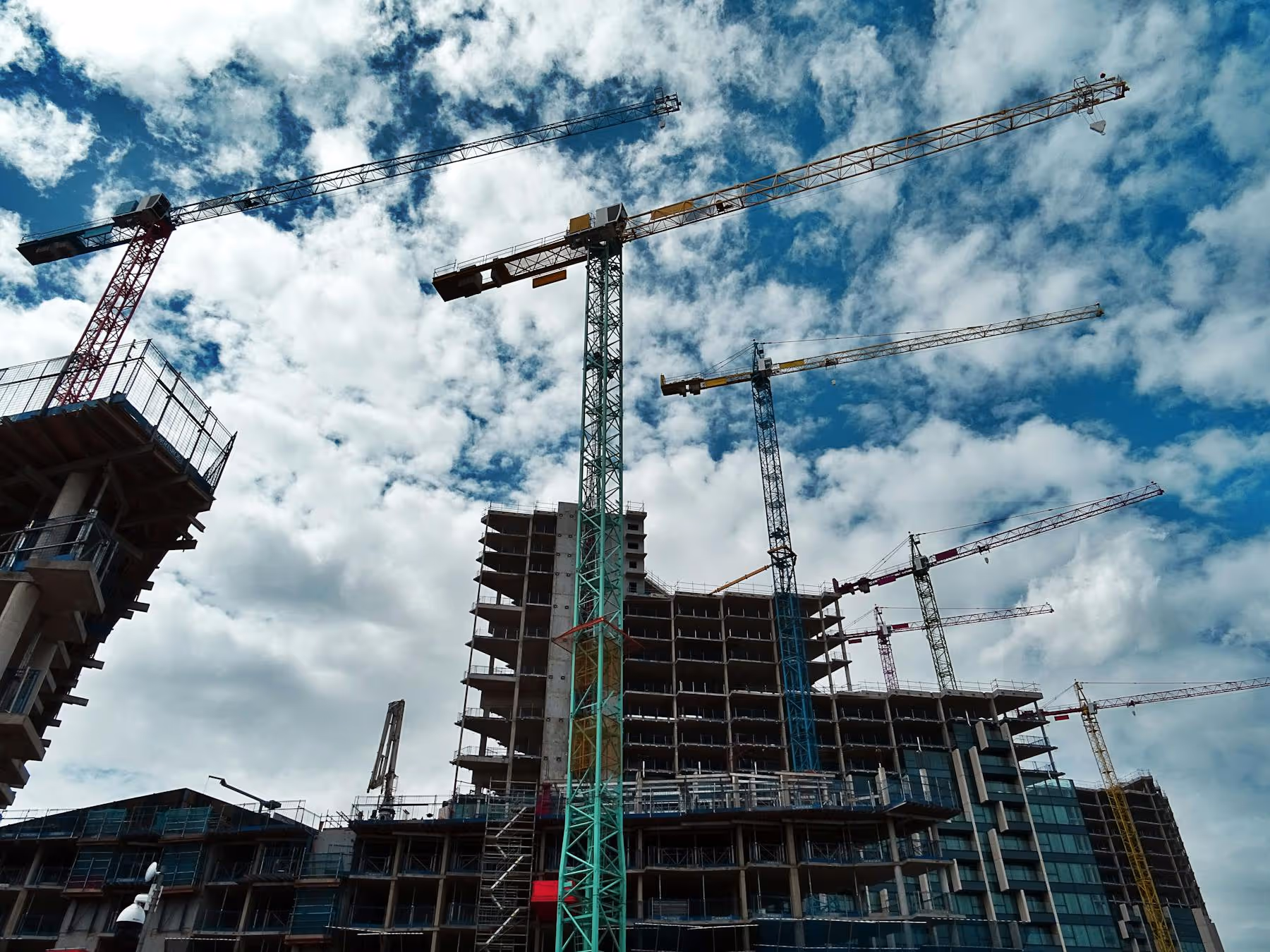 Urban construction site with multiple tower cranes framing rising skyscrapers under blue sky | Westside Construction Group