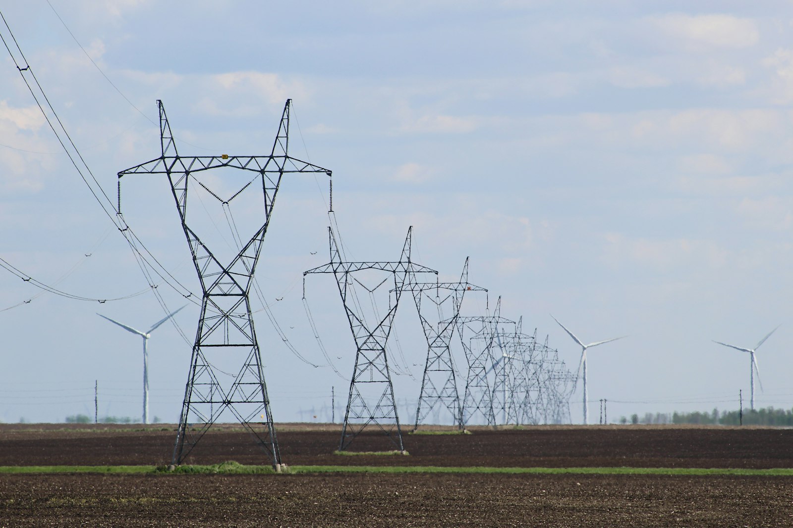 Transmission towers and wind turbines standing in an open field | Westside Construction Group