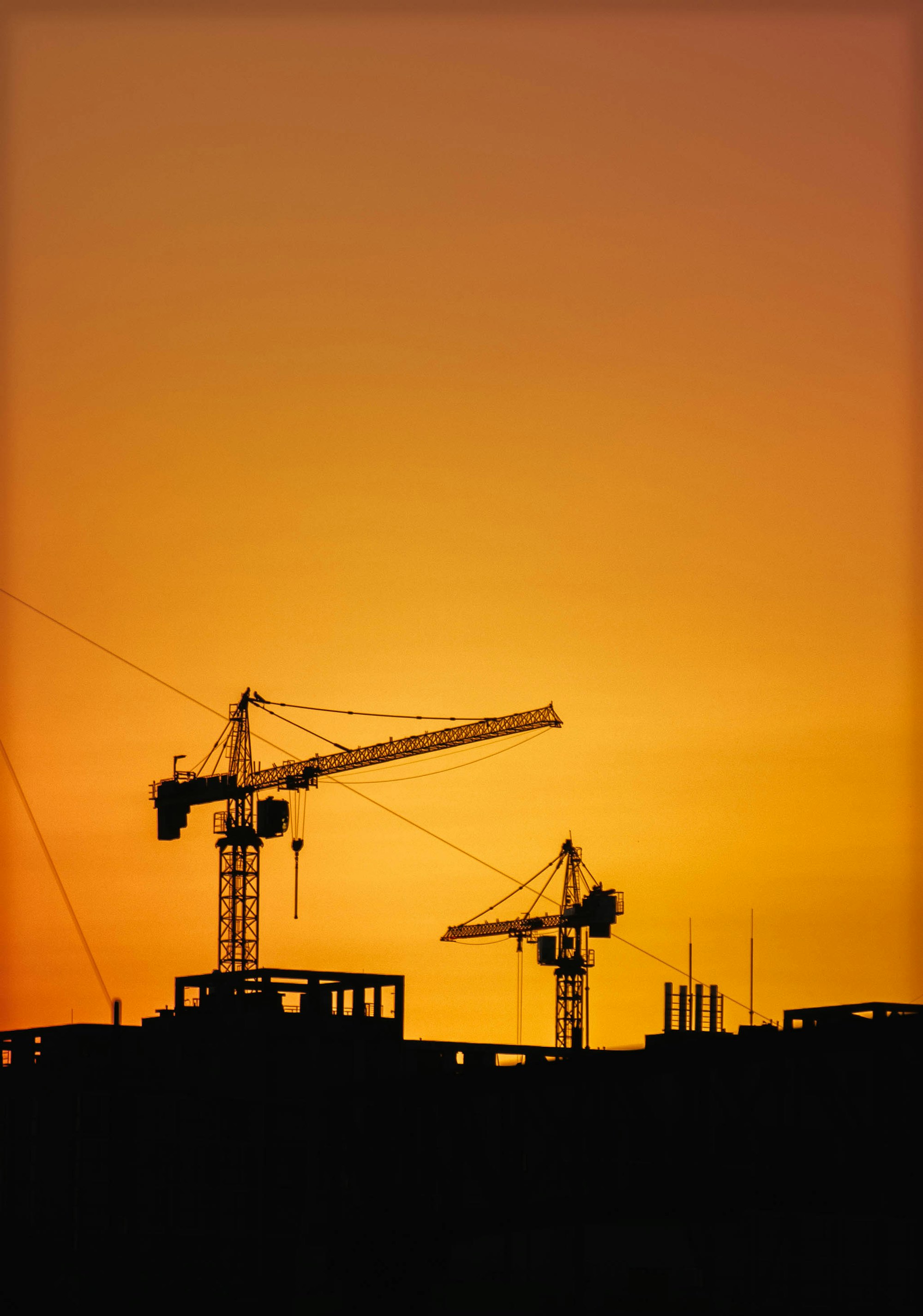 Construction cranes silhouetted against an orange sunset sky | Westside Construction Group