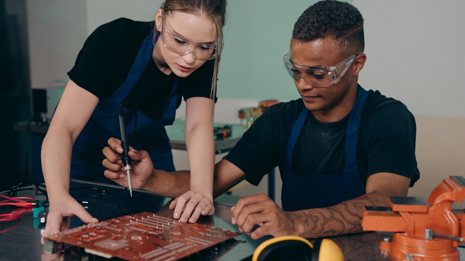 Two electronics engineers comparing and testing a printed circuit board at a workbench.
