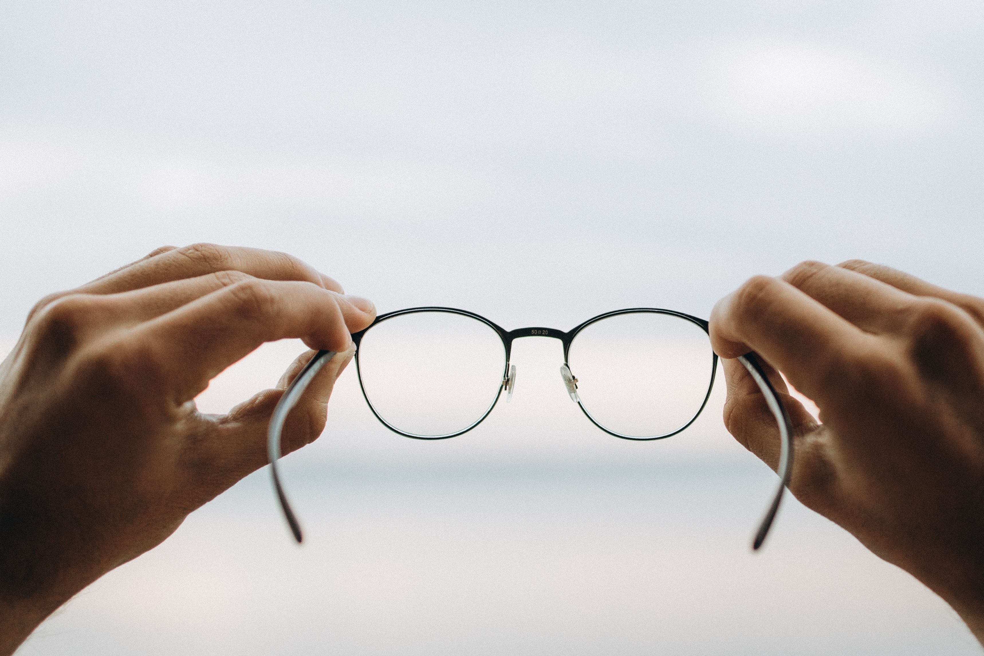 Black-framed eyeglasses held in front of a seascape. Illustrative stock, not TDK's prototype.