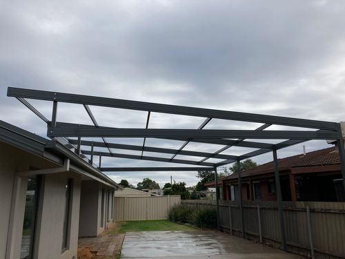 Metal frame structure for a patio attached to a house on a cloudy day.