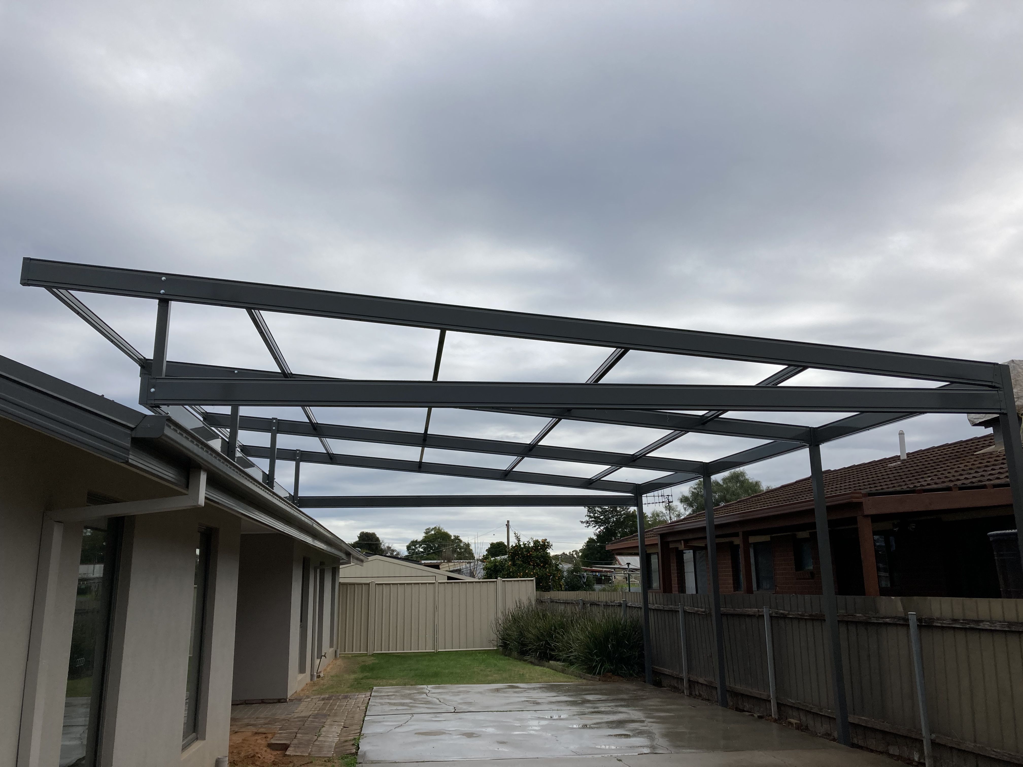 Metal frame structure for a patio attached to a house on a cloudy day.