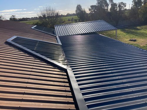 View of metal roofs with corrugated panels under sunlight and trees in the background.