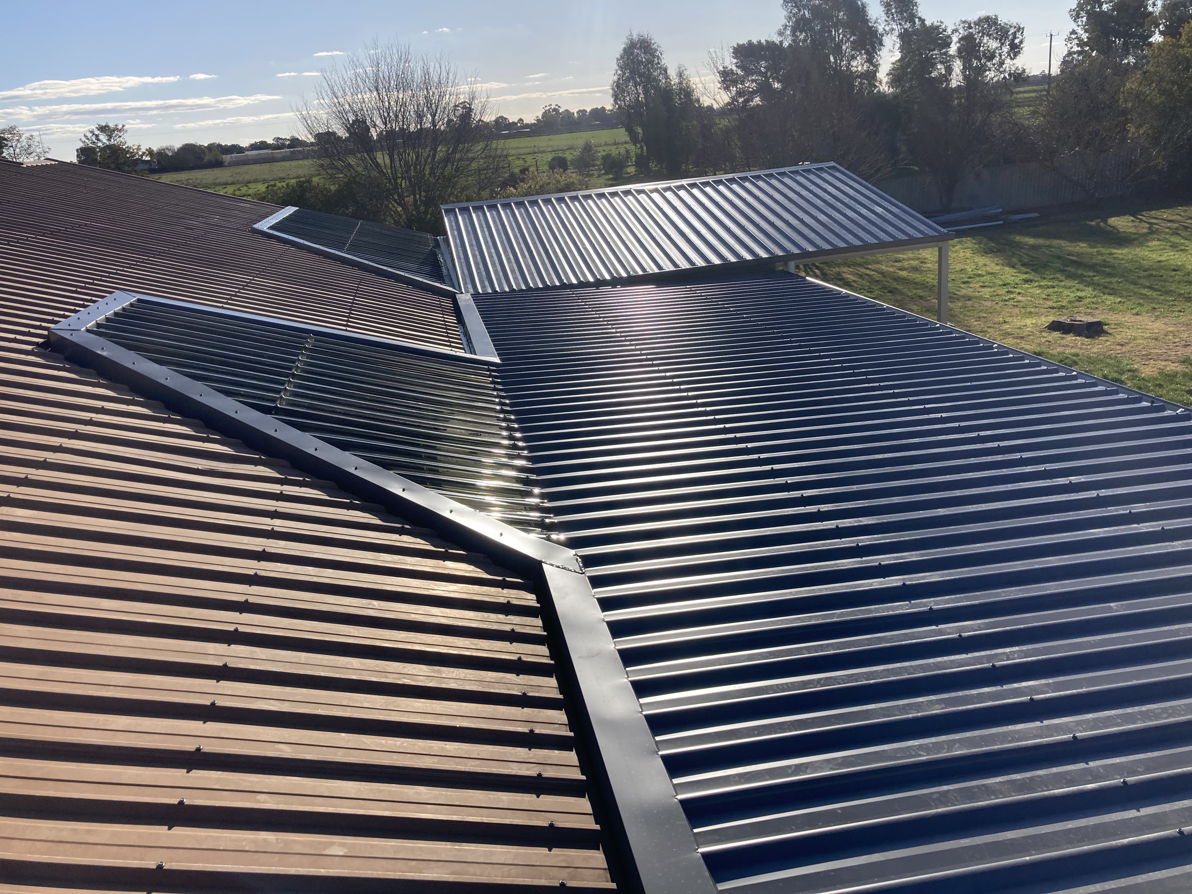 View of metal roofs with corrugated panels under sunlight and trees in the background.