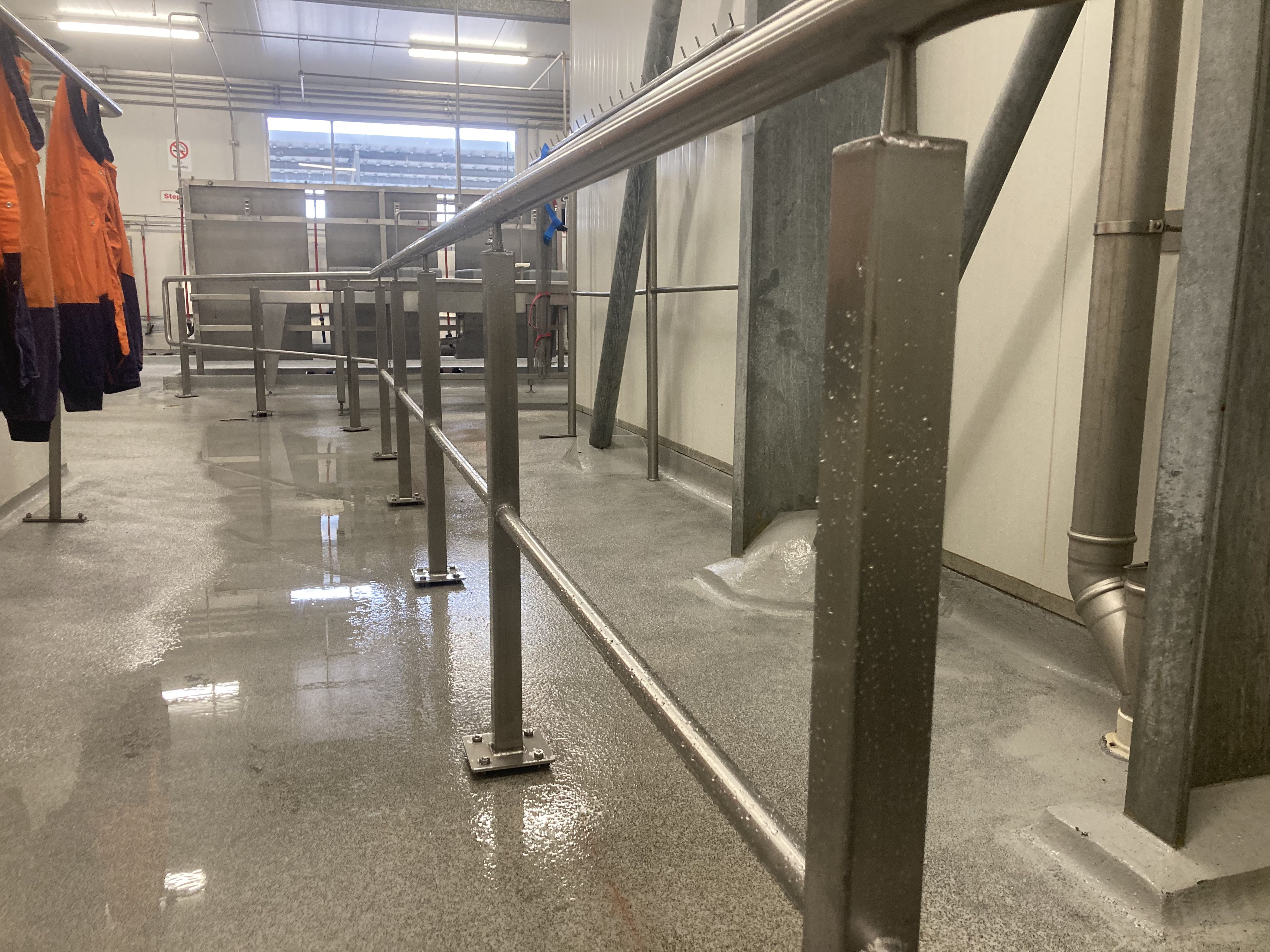 Industrial room with wet floor, metal railings, pipes, and orange protective jackets hanging on the left.