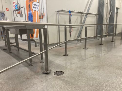 Industrial stainless steel railings and a sink in a clean factory setting with safety signage on the wall.