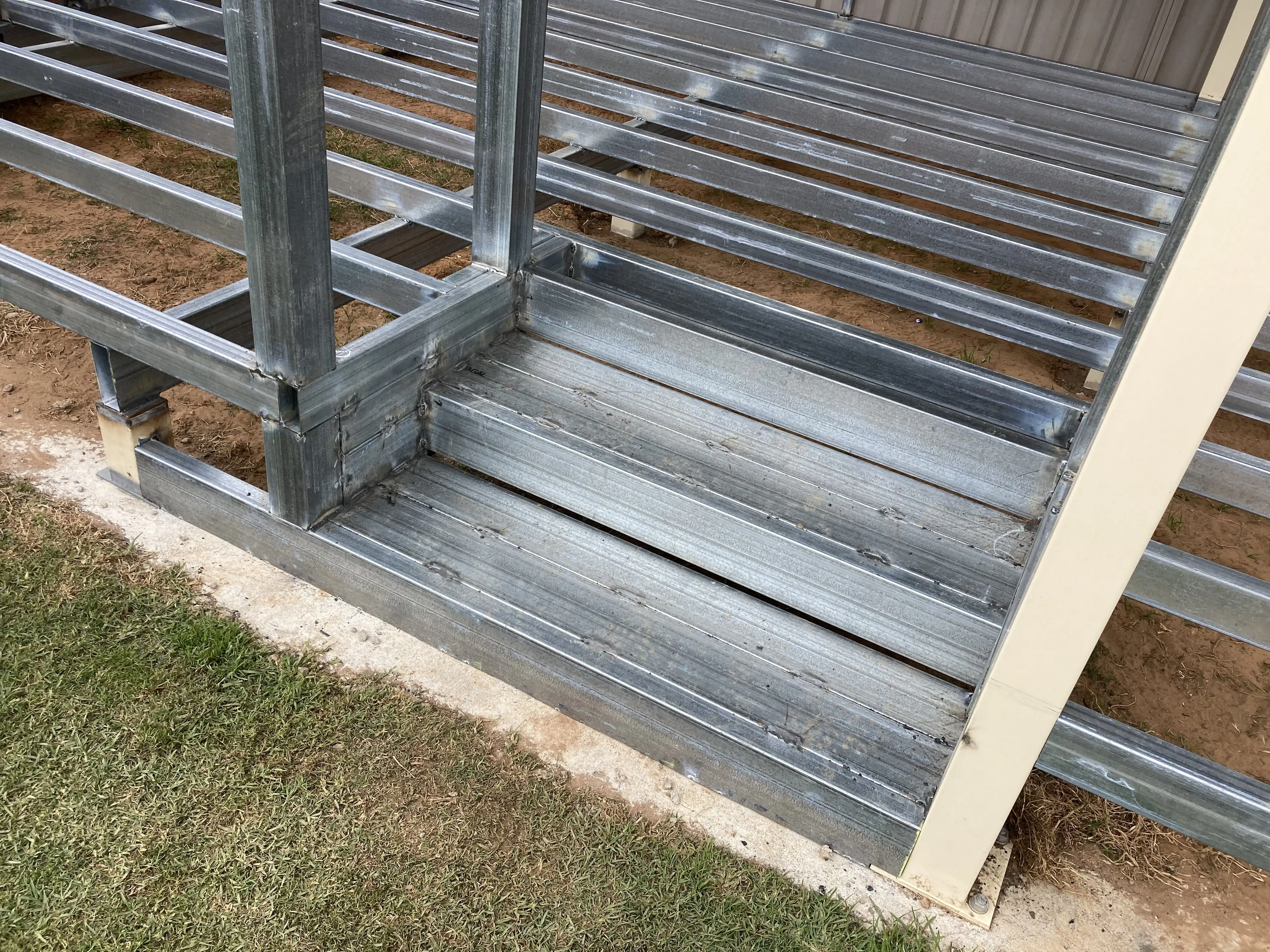 Close-up of metallic galvanized steel framework with horizontal beams on ground by grass.