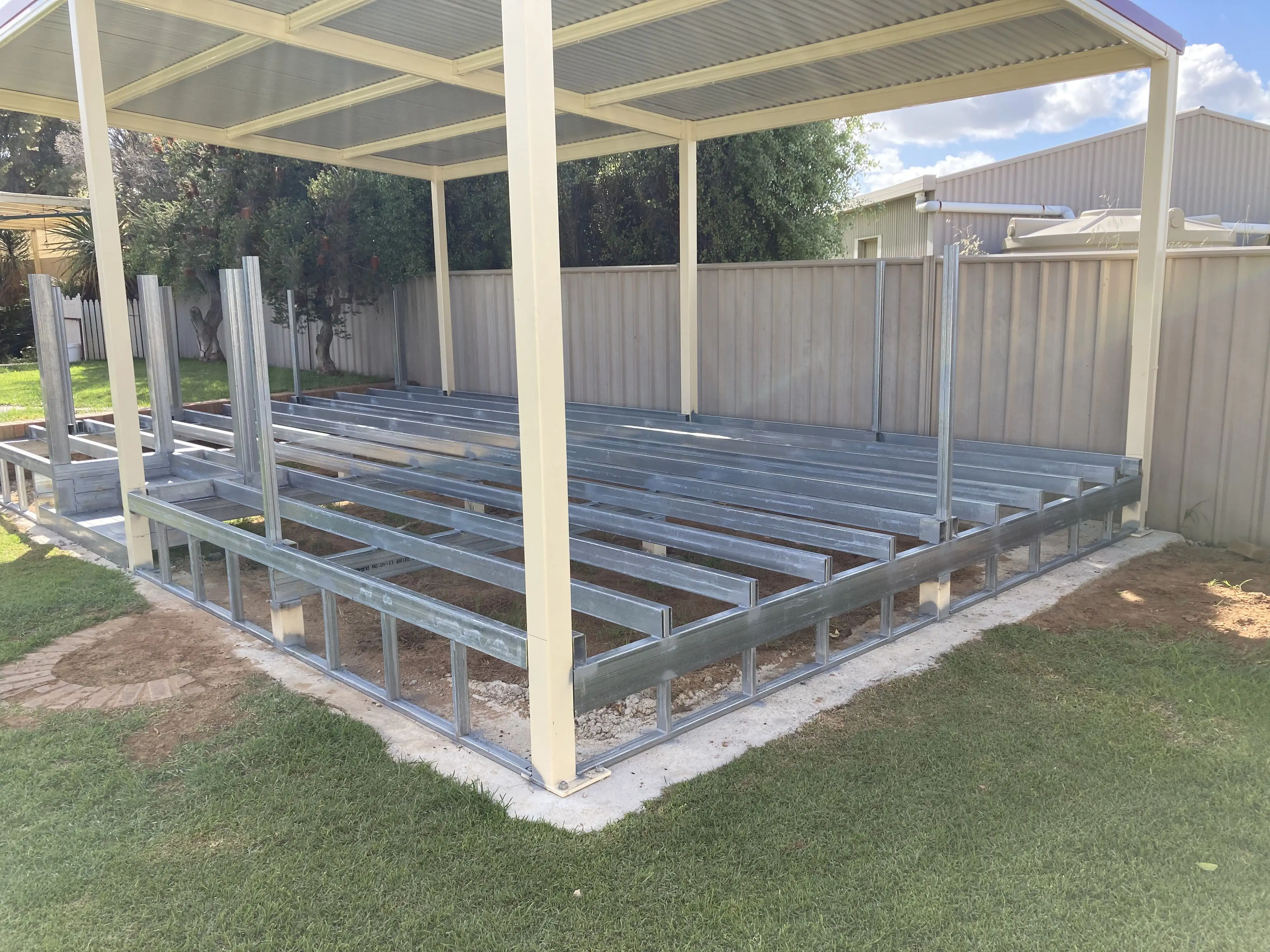 Metal frame construction of a patio or deck under a metal roof structure in a backyard.