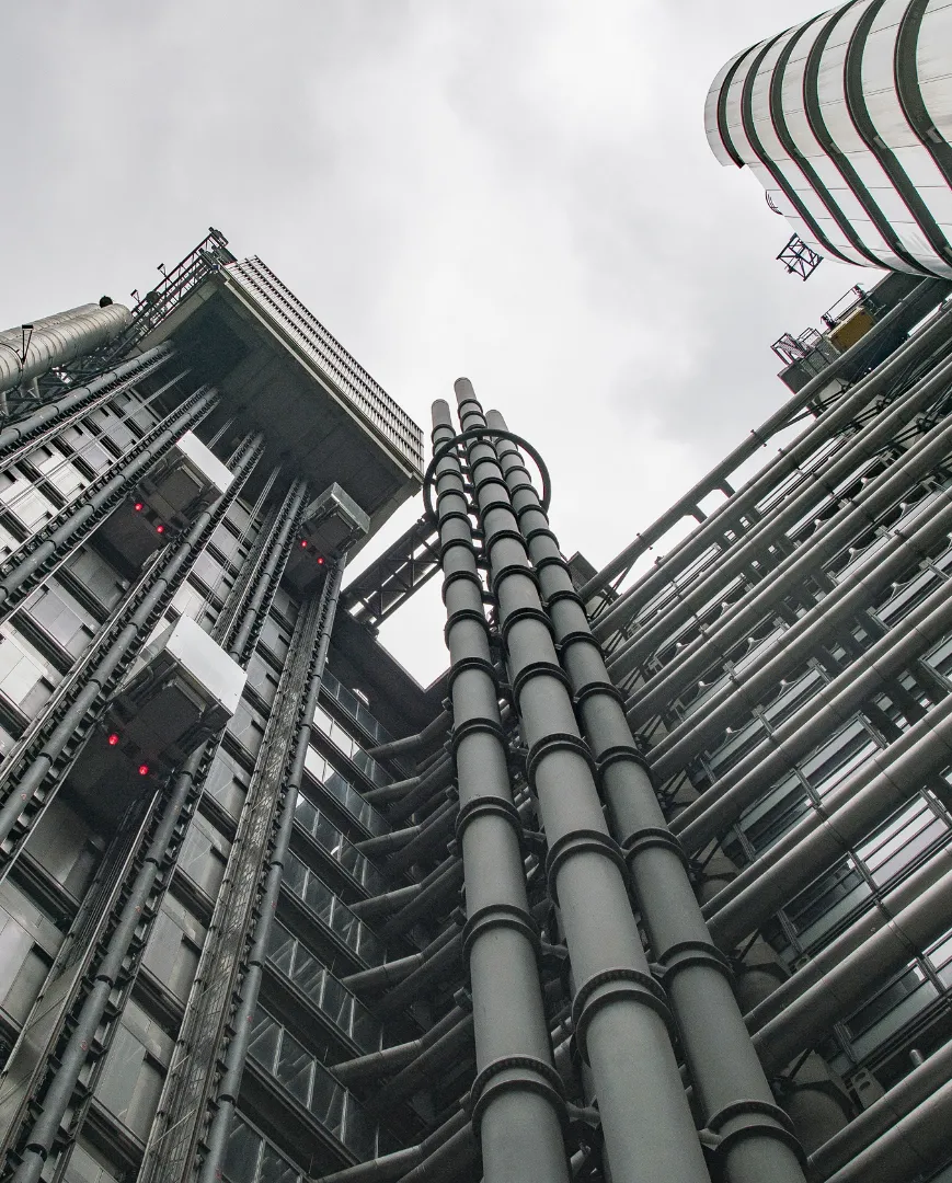 Low-angle view of industrial pipework against tall buildings
