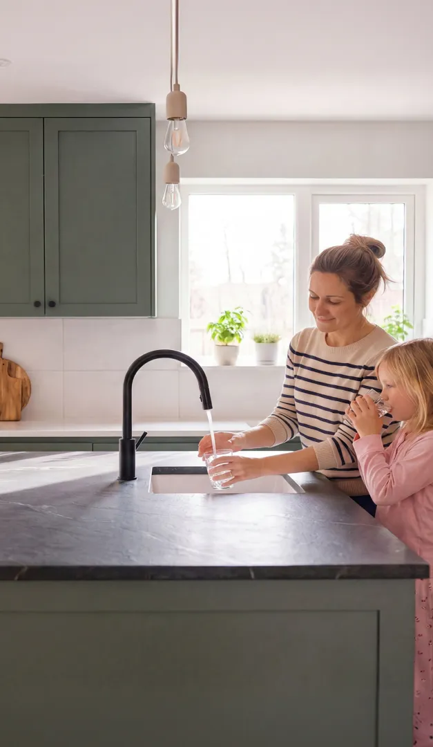 Mother filling a glass with tap water for her daughter at a kitchen sink