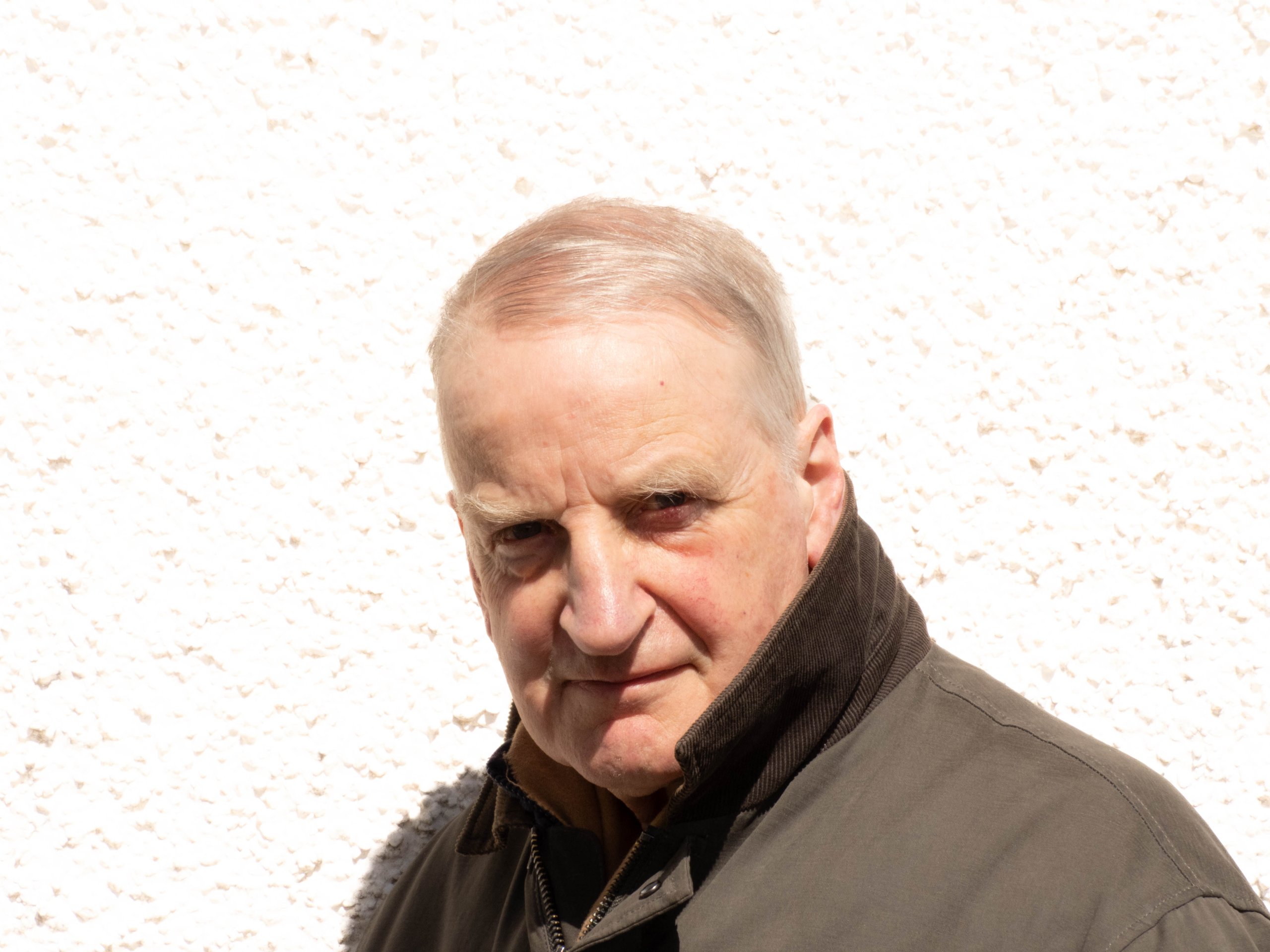 Close-up of an older man with short hair wearing a dark jacket with a turned-up collar.
