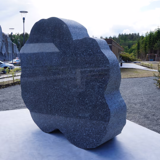 Stor, svart, glatt skulptur i uvanlig form plassert på en betongflate utendørs.