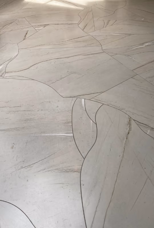 Detaljbilde av lys marmorflislagt gulv med naturlige sprekker og mønstre.