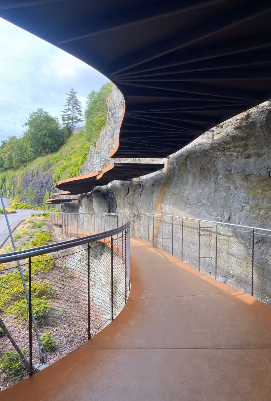 Gangvei med buet bratt rekkverk langs fjellside med svingete tak over gangvei.