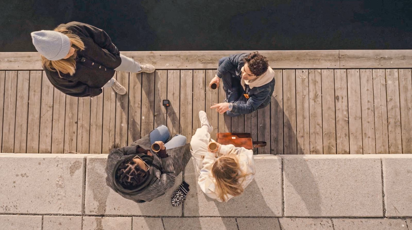 Four people recording a conversation outdoors on a wooden dock by the water