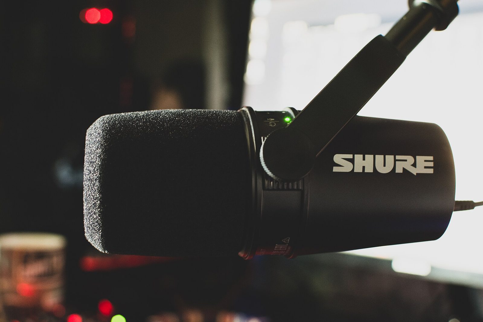 Shure MV7 podcast microphone with foam windscreen mounted on a boom arm, side view with the Shure logo