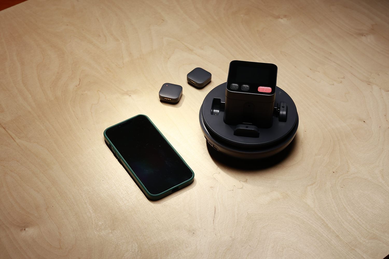 Space Recorder on its charging base next to two small wireless mics and a smartphone on a light wooden table.