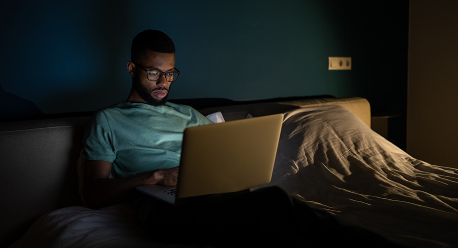 a man sitting on a bed using a laptop computer