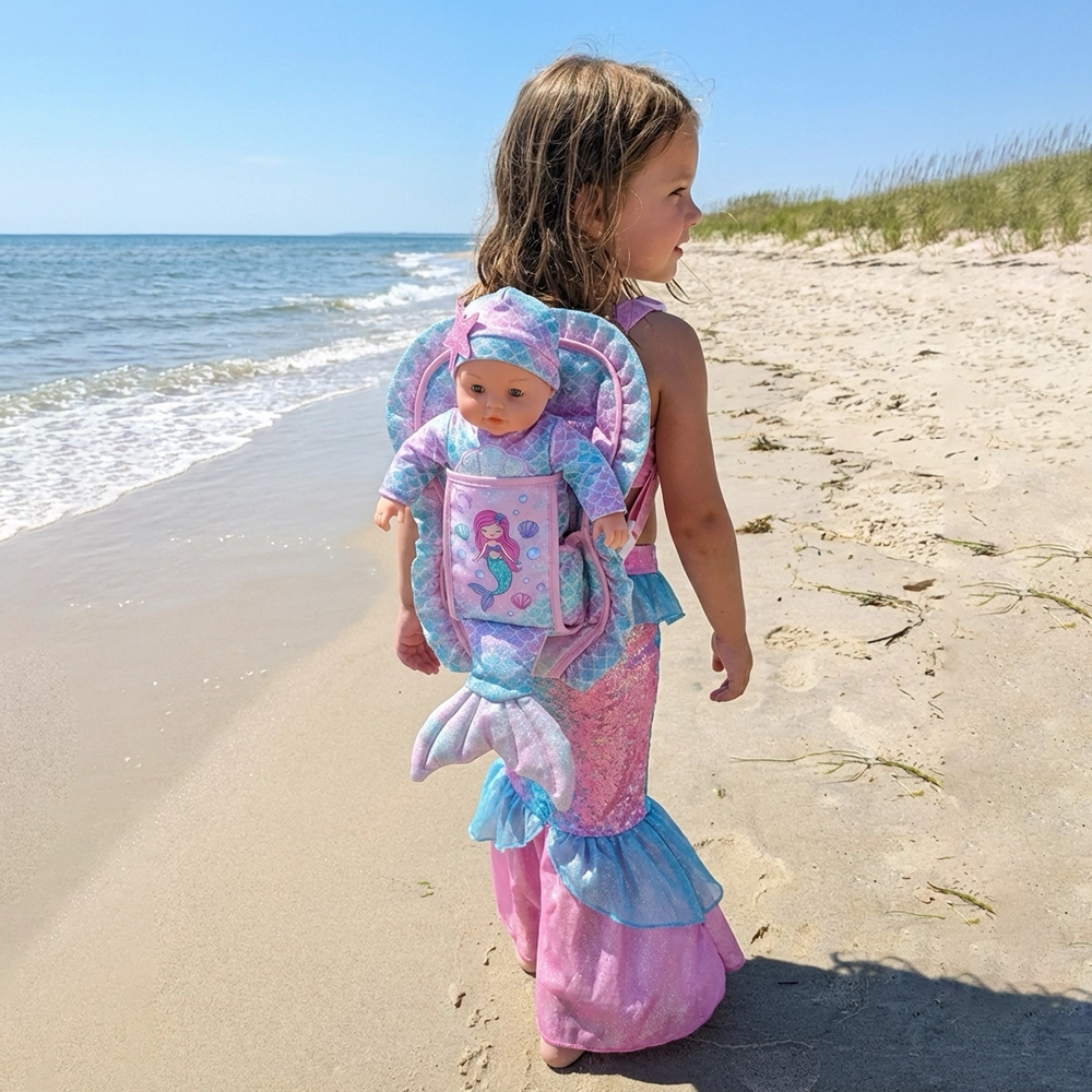 Little girl in a mermaid costume with a mermaid doll in a matching backpack walking on the beach.