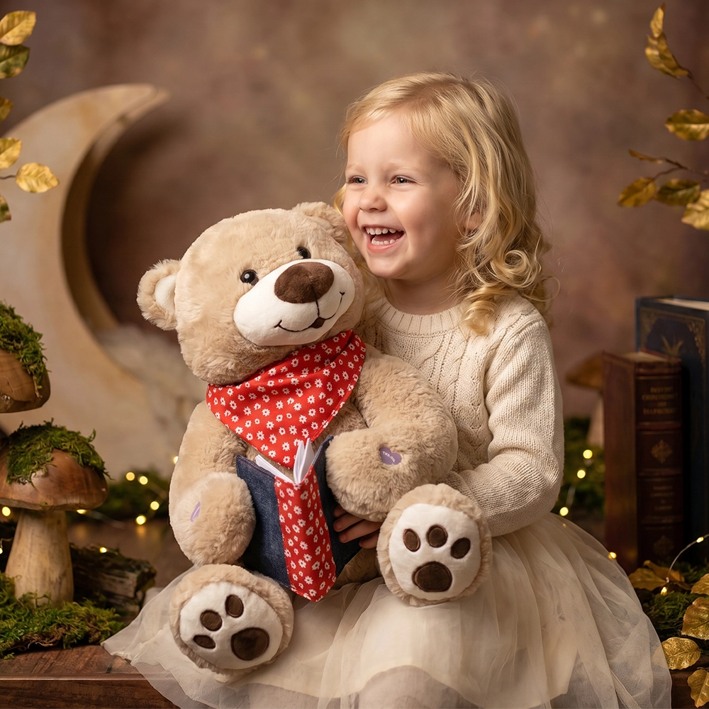 Smiling blonde girl hugging a teddy bear wearing a red scarf and holding a book.