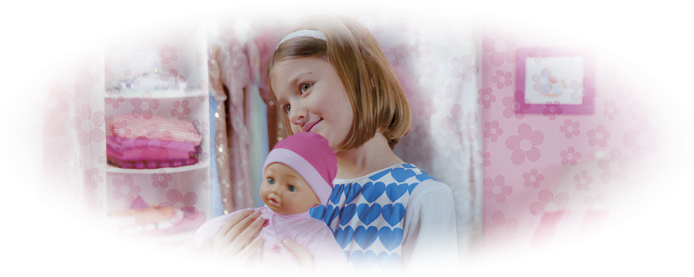 Young girl in blue heart dress holding and looking at a baby doll in pink outfit and hat.