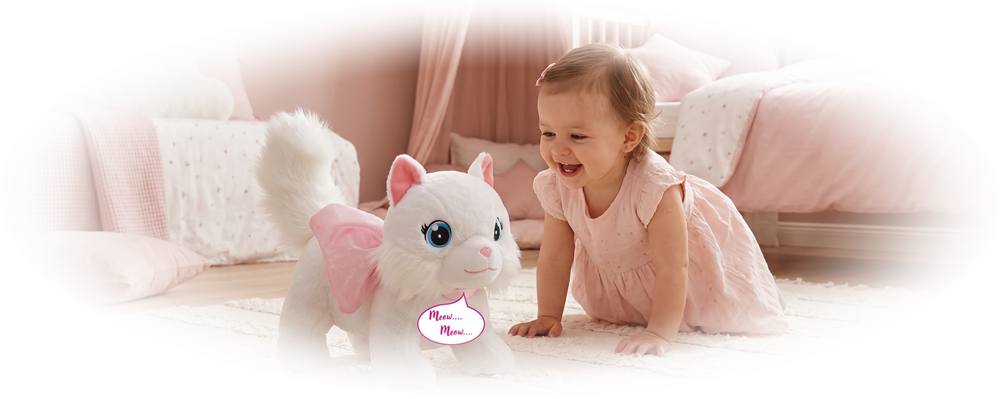 Toddler girl in pink dress smiling at a white plush cat toy with pink wings on a cream rug.