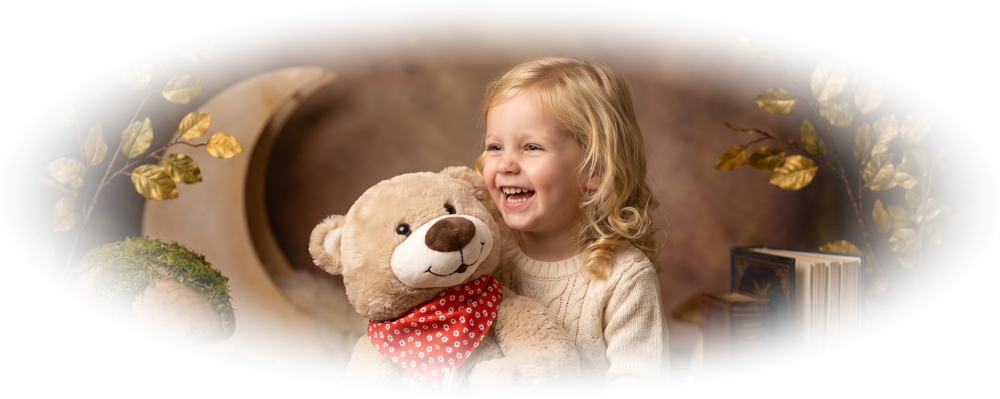 Smiling blonde girl hugging a teddy bear wearing a red scarf and holding a book.