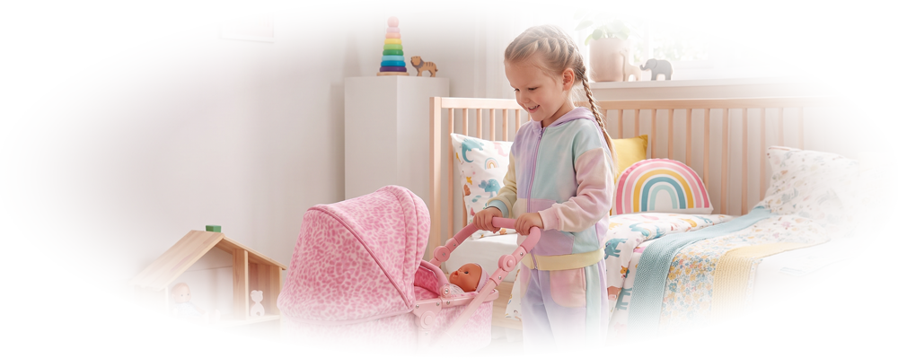 Smiling girl pushing a pink toy stroller with a doll inside in a colorful children's bedroom.