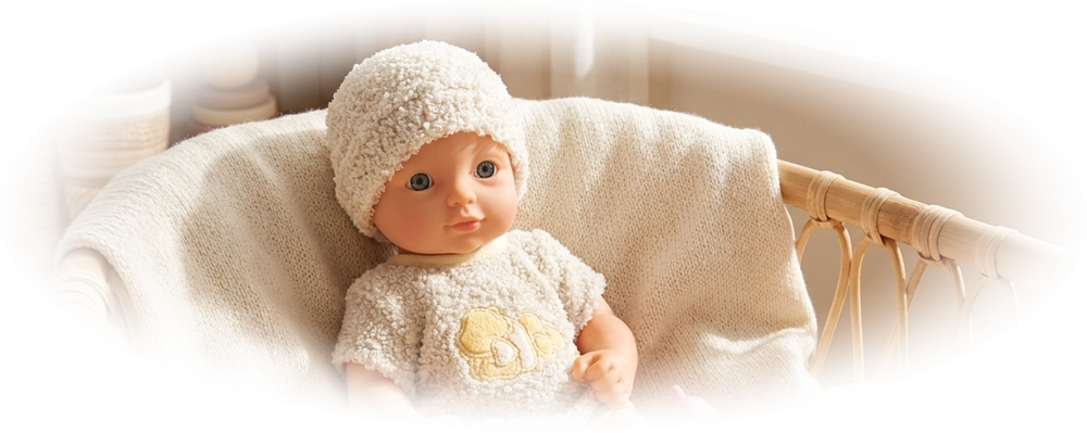 Baby doll wearing textured outfit and hat, lying in wicker bassinet with pink bottle beside it.