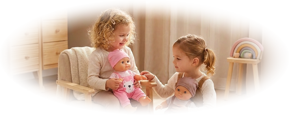 Two young girls playing with baby dolls in a cozy, softly lit room with wooden furniture and toys.