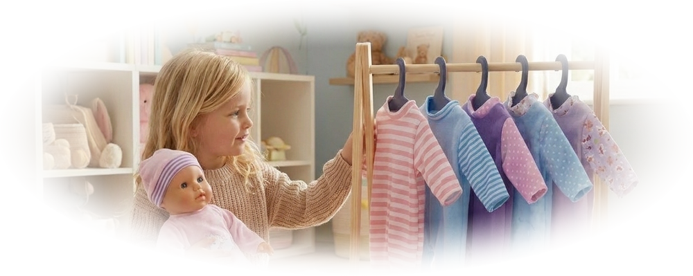 A girl sitting on a rug holding a baby doll with striped pajamas hanging on a wooden rack.