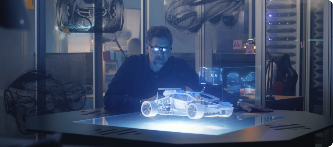 Man wearing glasses studies a glowing 3D hologram of a car on a table in a dark room.