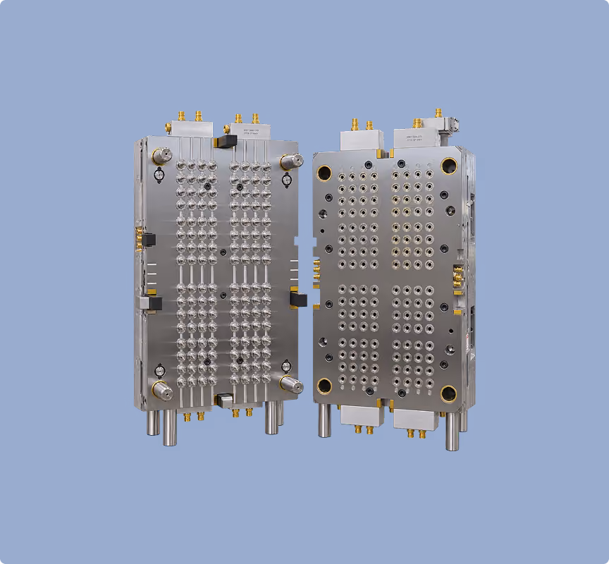 Two metallic industrial molds with multiple circular cavities and connectors, facing each other, on a solid blue background.