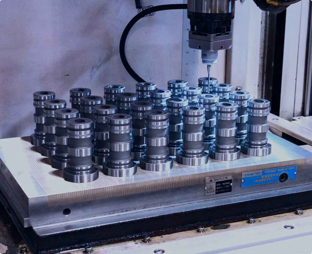 Rows of identical metallic cylindrical parts arranged on a flat machine surface, with a precision measuring tool positioned above them, likely used for quality inspection or machining.
