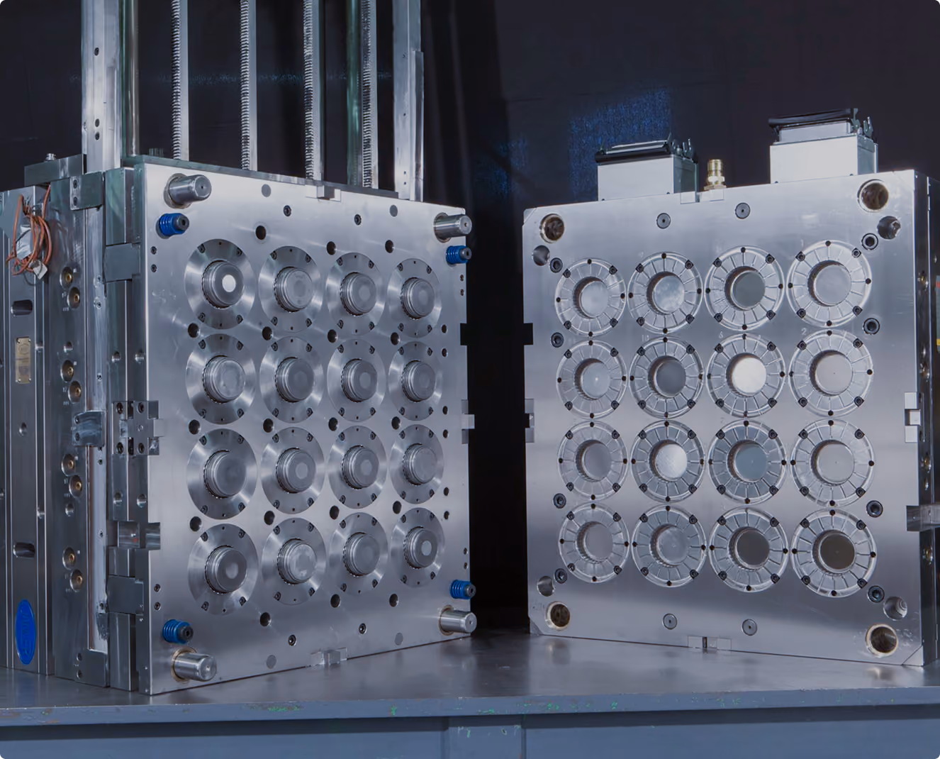 Two large shiny metal injection mold halves placed side by side on a workbench, designed for molding multiple round objects simultaneously.