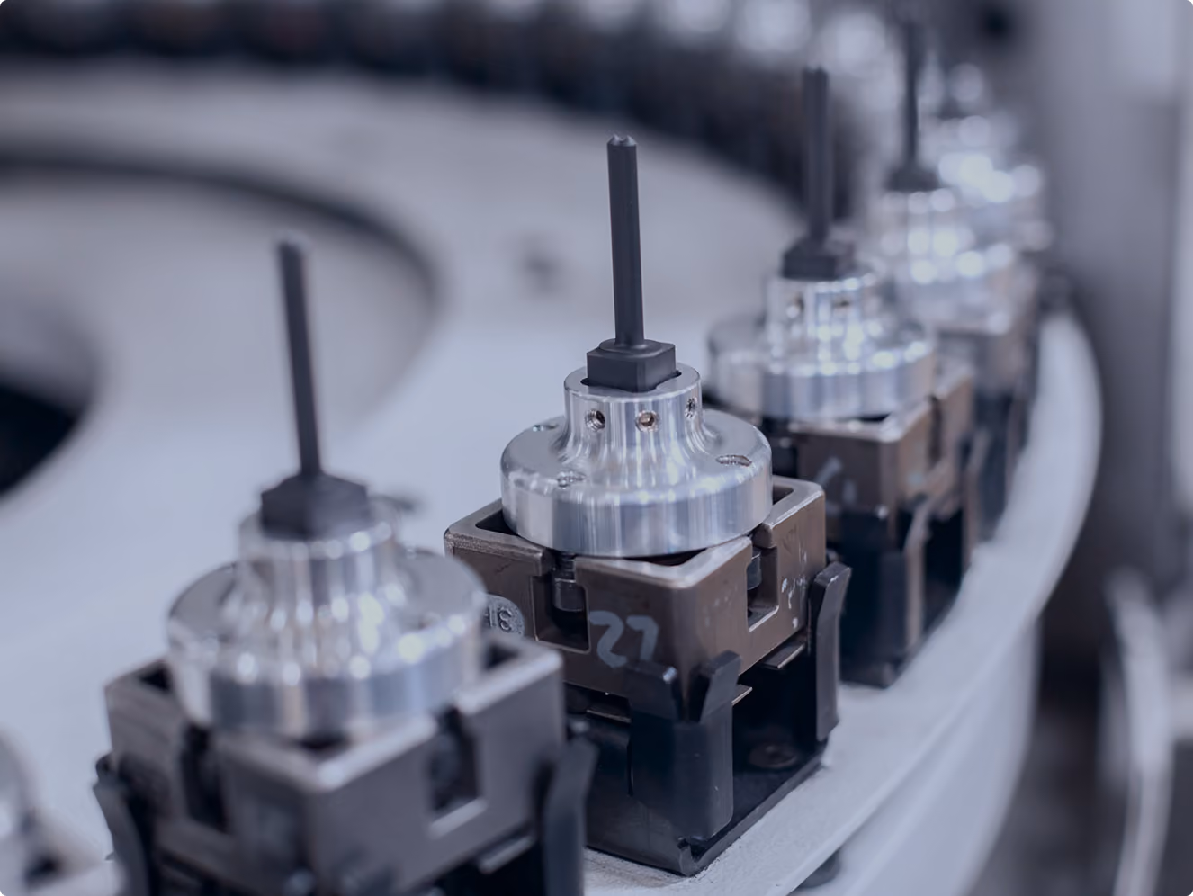 Close-up of a row of metal precision tool holders with black shank bits arranged on a curved industrial machine track.