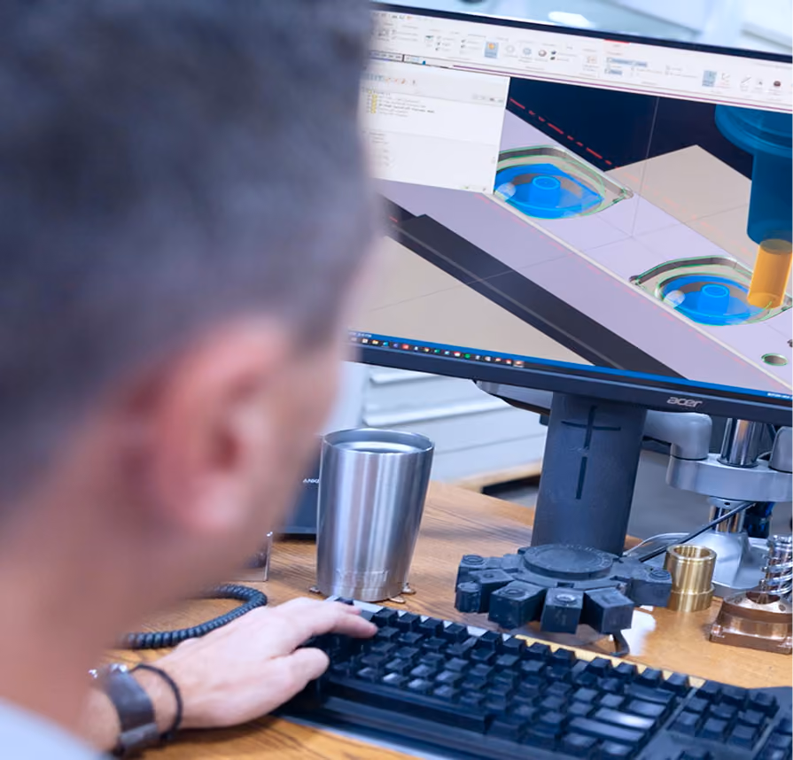 Person working at a desk using CAD software on a computer to design a 3D model of mechanical parts.